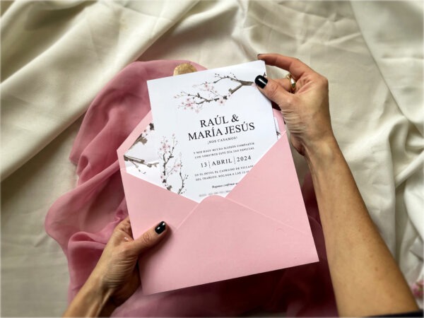 Detalle de la invitación de boda sakura con flores de cerezo siendo sostenida en la mano.