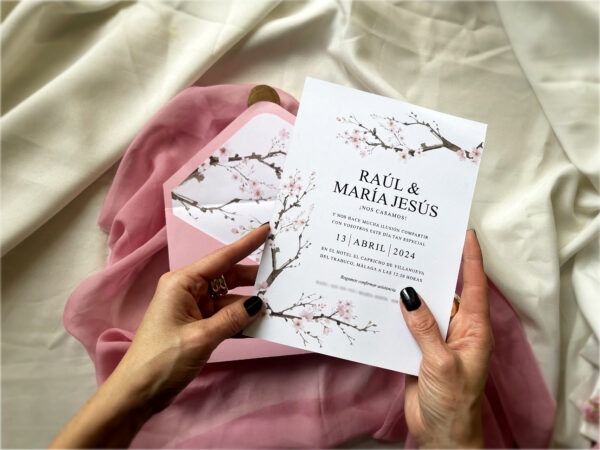 Detalle de la invitación de boda sakura con flores de cerezo siendo sostenida en la mano.