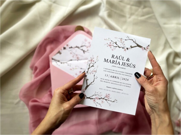 Detalle de la invitación de boda sakura con flores de cerezo siendo sostenida en la mano.