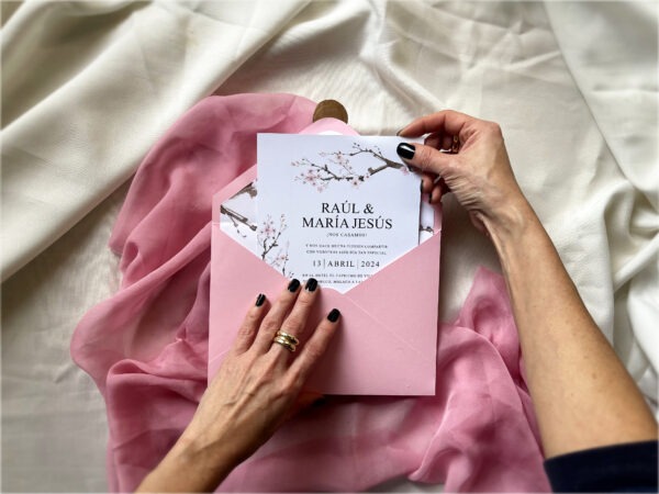 Detalle de la invitación de boda sakura con flores de cerezo siendo sostenida en la mano.