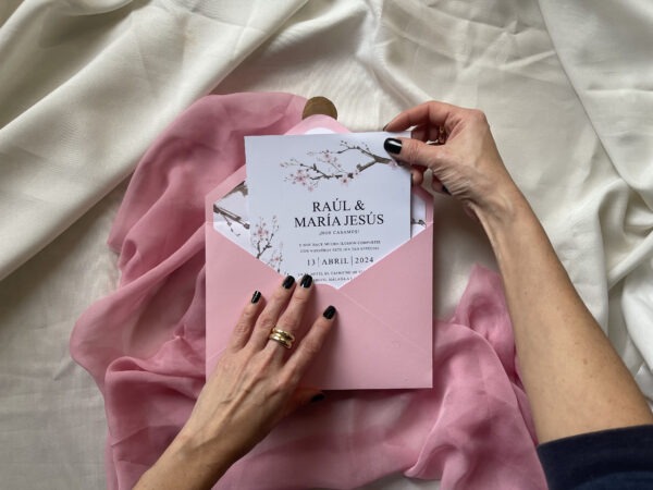 Detalle de la invitación de boda sakura con flores de cerezo siendo sostenida en la mano.
